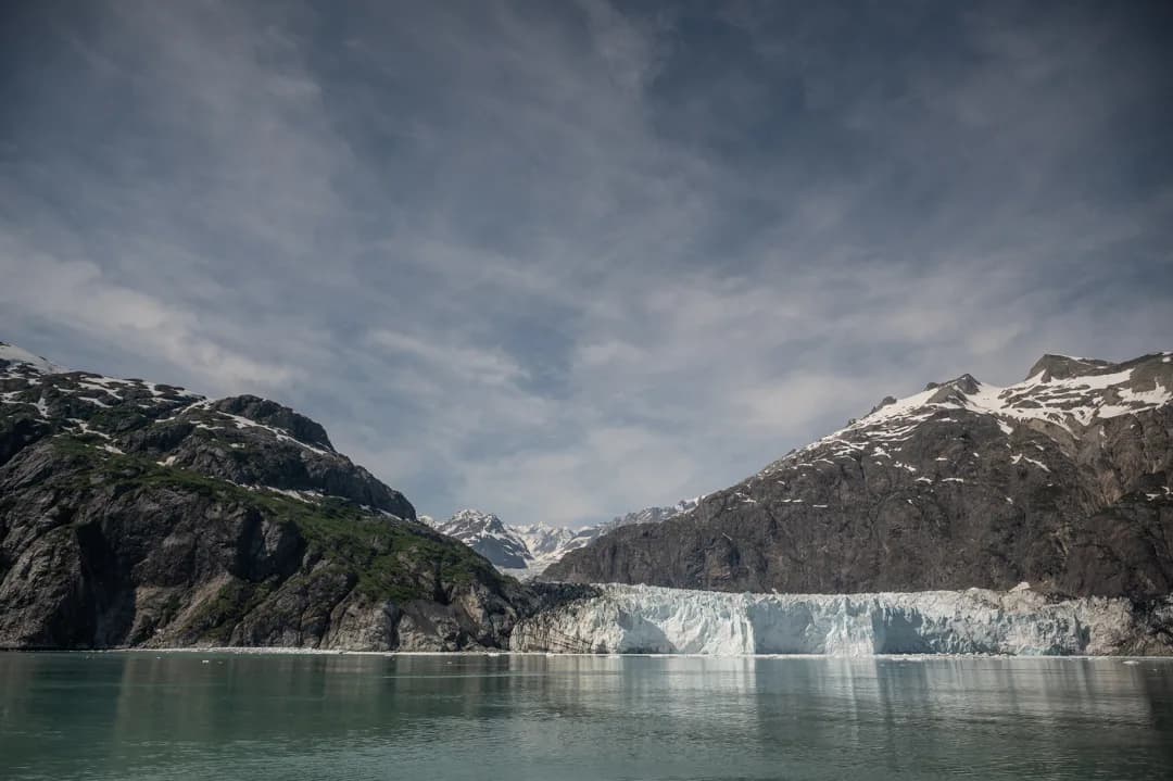 Tidewater glacier calving face meets turquoise water between snow-capped peaks in Glacier Bay, Alaska