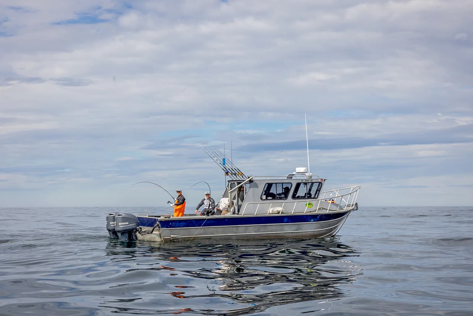 Aluminum charter boat with anglers fishing from the stern on calm open water under a partly cloudy sky.