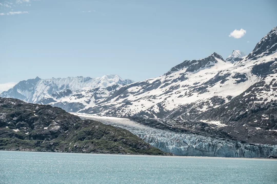 Tidewater glacier descending to glacial blue water, snow-covered peaks rising behind, Glacier Bay National Park.