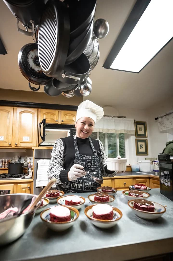 Chef in white toque plating individual red velvet cake desserts with chocolate sauce in lodge kitchen