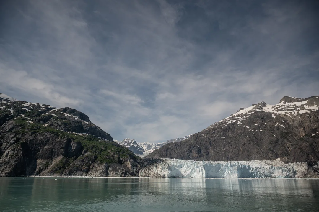 Tidewater glacier calving face meets turquoise water between snow-capped peaks in Glacier Bay, Alaska