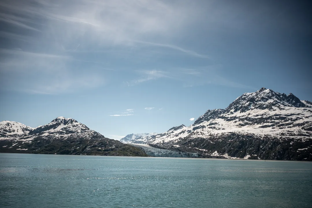 Snow-capped mountains flank a tidewater glacier descending to calm turquoise water in Glacier Bay
