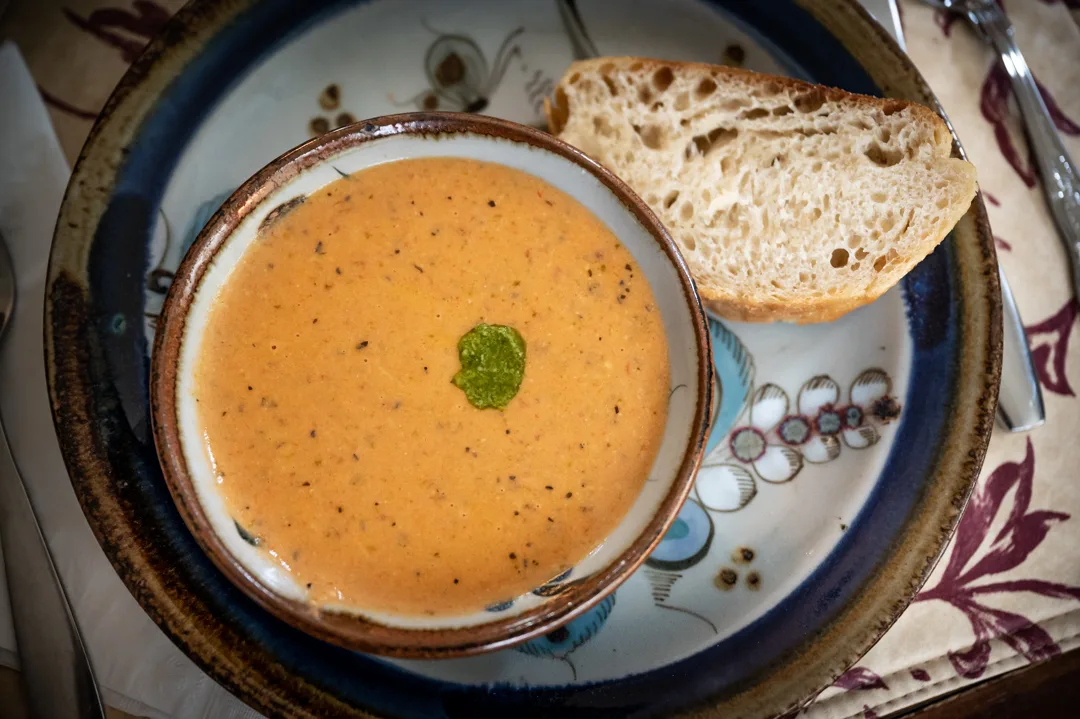 Bowl of creamy tomato bisque with herb garnish and crusty bread slice on a floral ceramic plate.