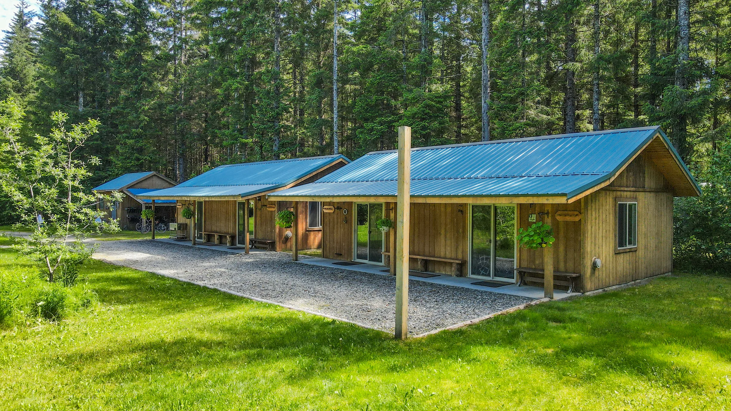 Row of wood-sided guest cabins with blue metal roofs and covered porches set against a spruce forest.